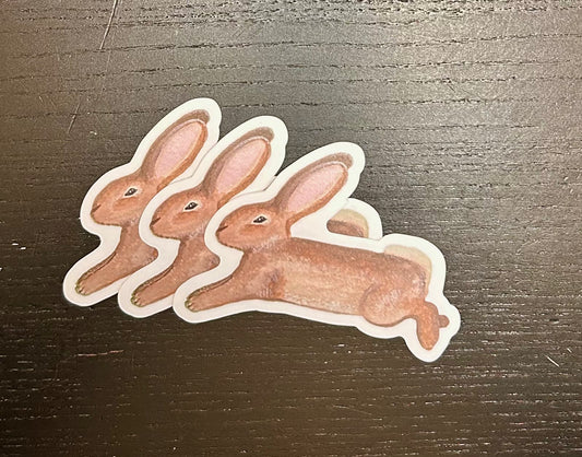 3 die-cut sticker of the Stella & Dorrie Leap bunny, matte finish, shown on back wooden table.
