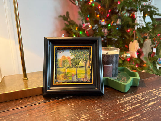 Framed artwork on a table with a decorated Christmas tree in the background
