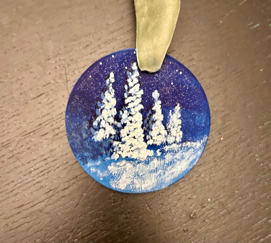 Original hand-painted round, flat ornament of snow-covered evergreens against a starry night sky.