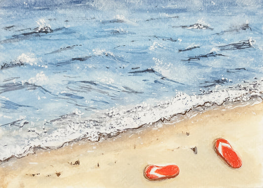 Two red flip-flops on a sandy beach with waves in the background