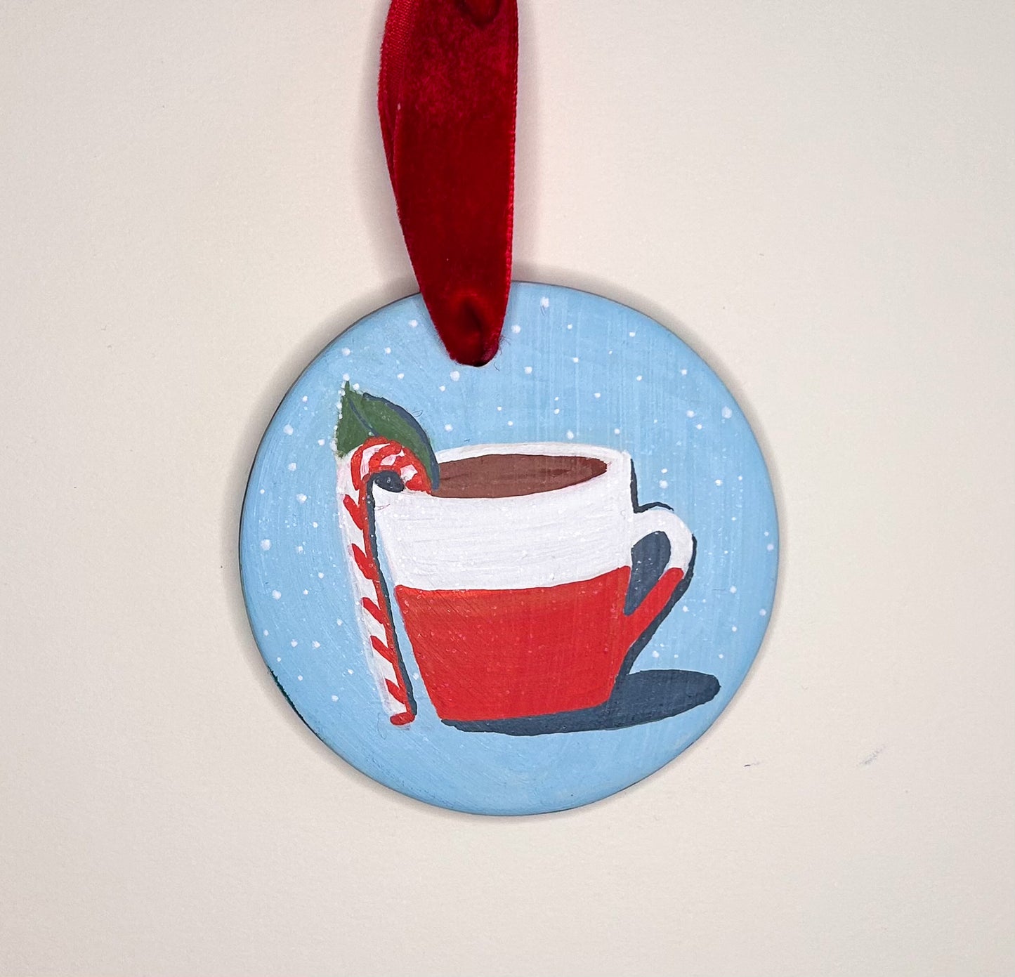 Original hand-painted bisque ceramic ornament of hot cocoa topped with a candy cane and mint leaf in a red-and-white mug, on a pale cyan background with tiny white dot details.