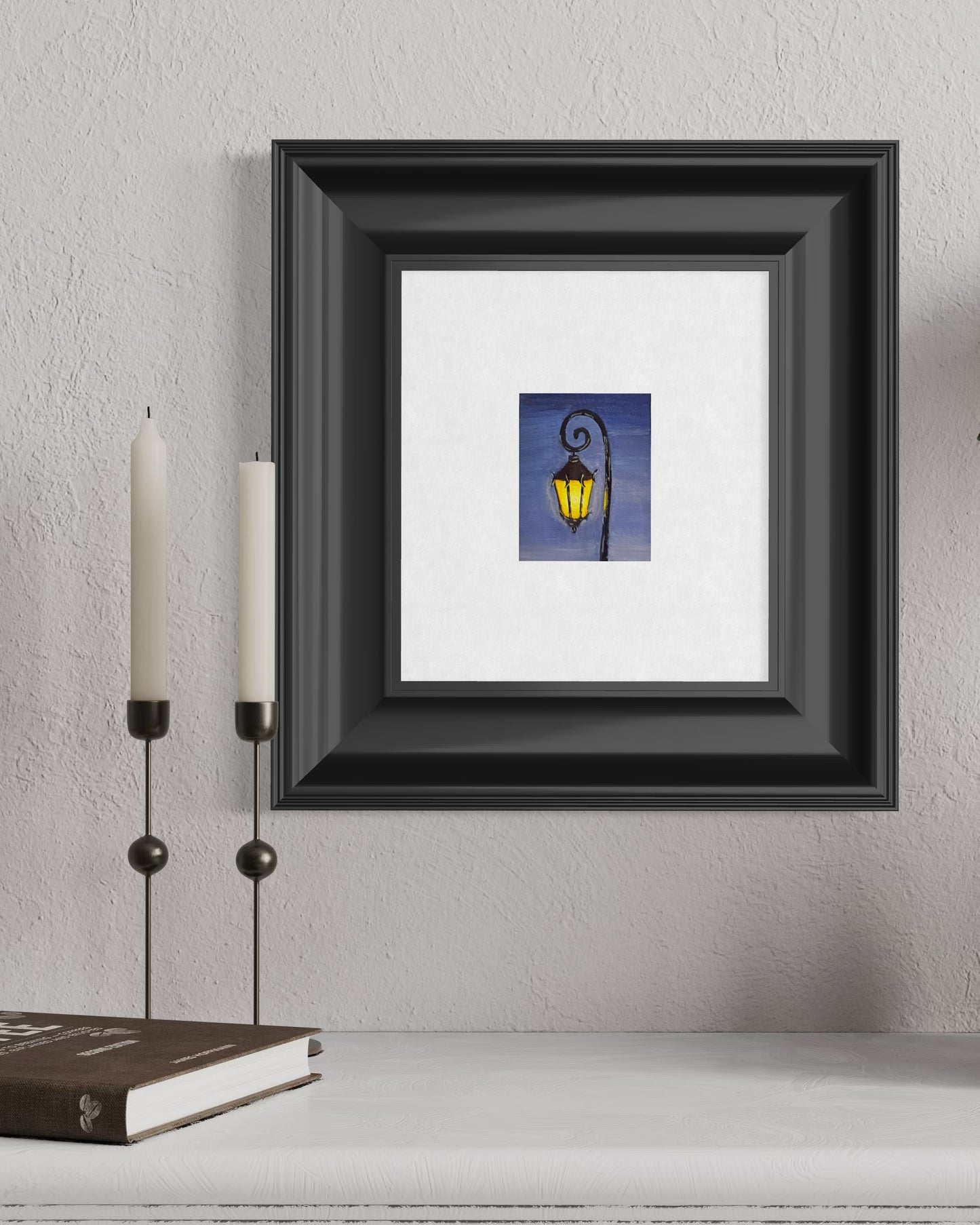 Framing mockup of artwork of a street lamp on a white wall with candles and a book.
