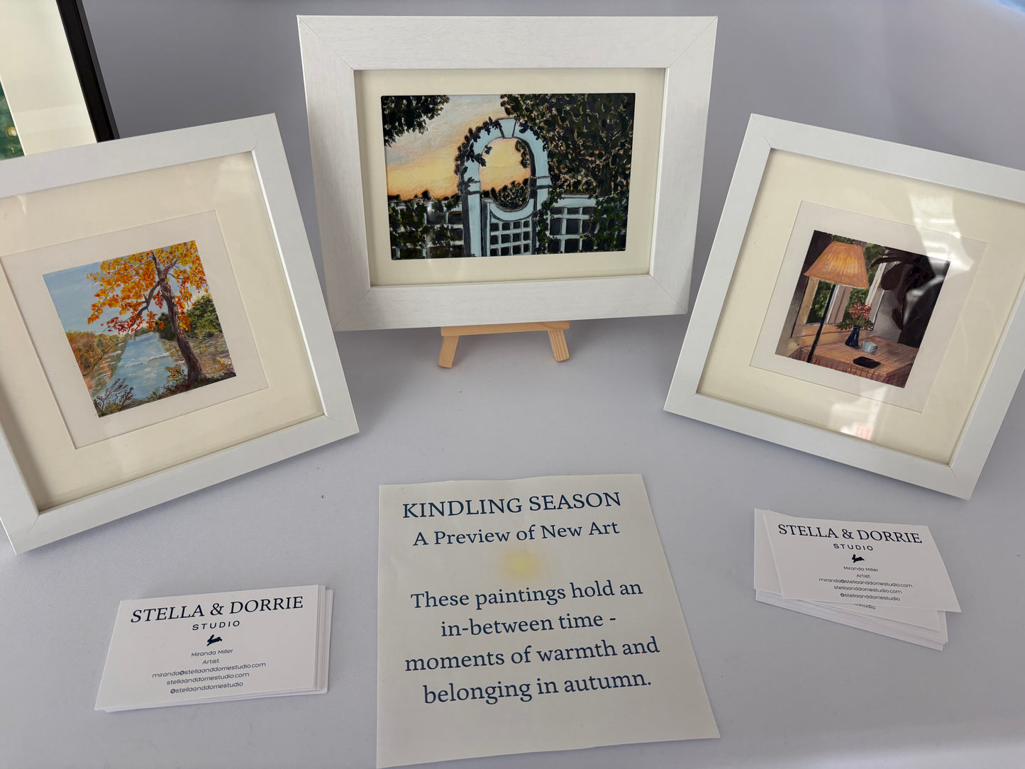 Three paintings from the Kindling Season Collection, including "Where the Swans Nest" matted in white frames.