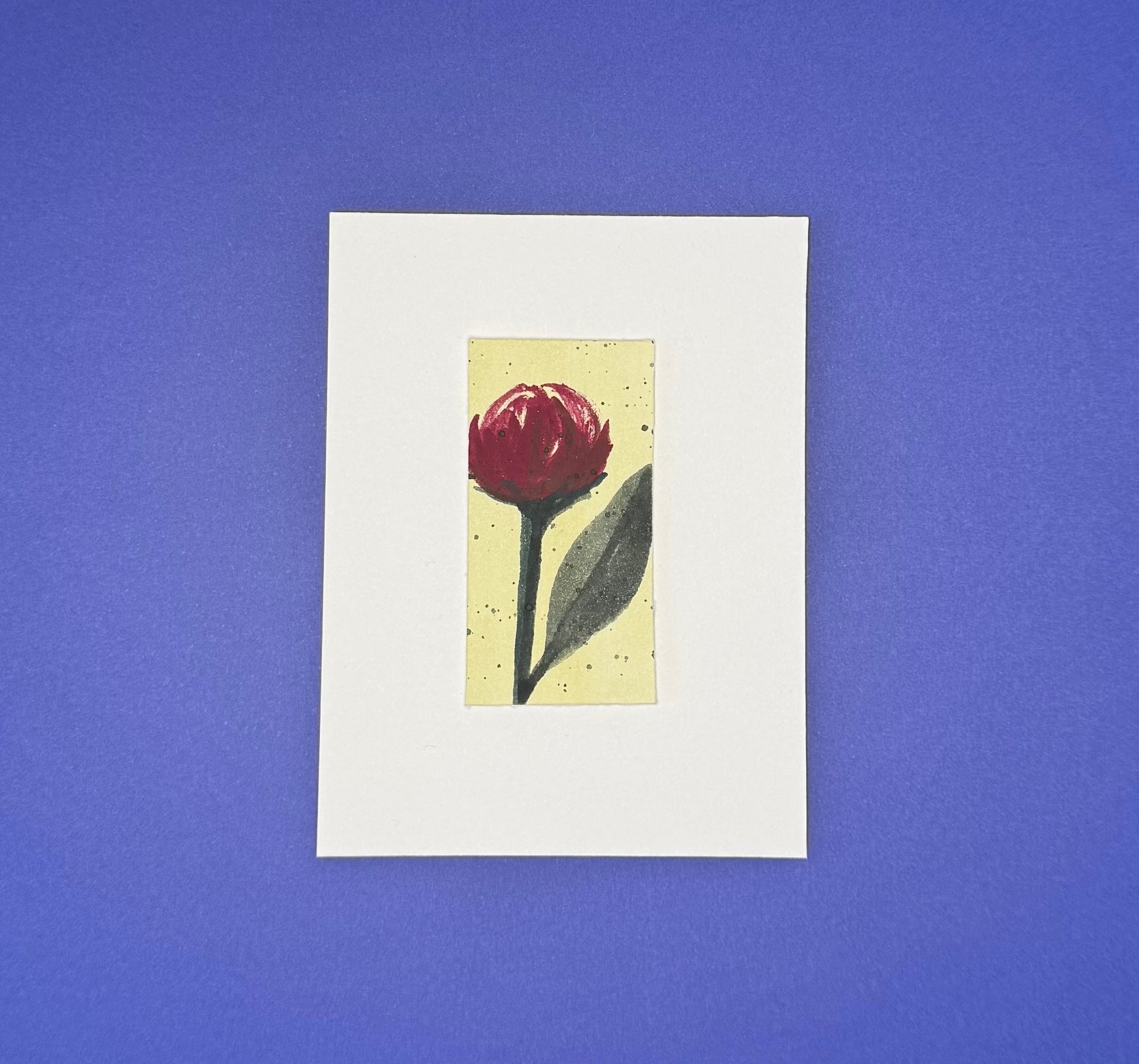 Small framed Stella & Dorrie Studio artwork of a burgundy flower with a creamy yellow background mounted on premium paper.