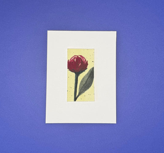 Small framed Stella & Dorrie Studio artwork of a burgundy flower with a creamy yellow background mounted on premium paper.