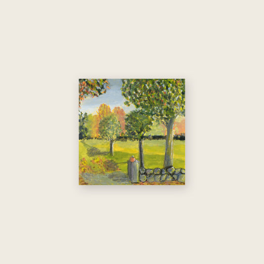 Small gouache painting of a pumpkin resting on a stone wall with autumn trees and a golden field; shown with a white paper border on a cream background.