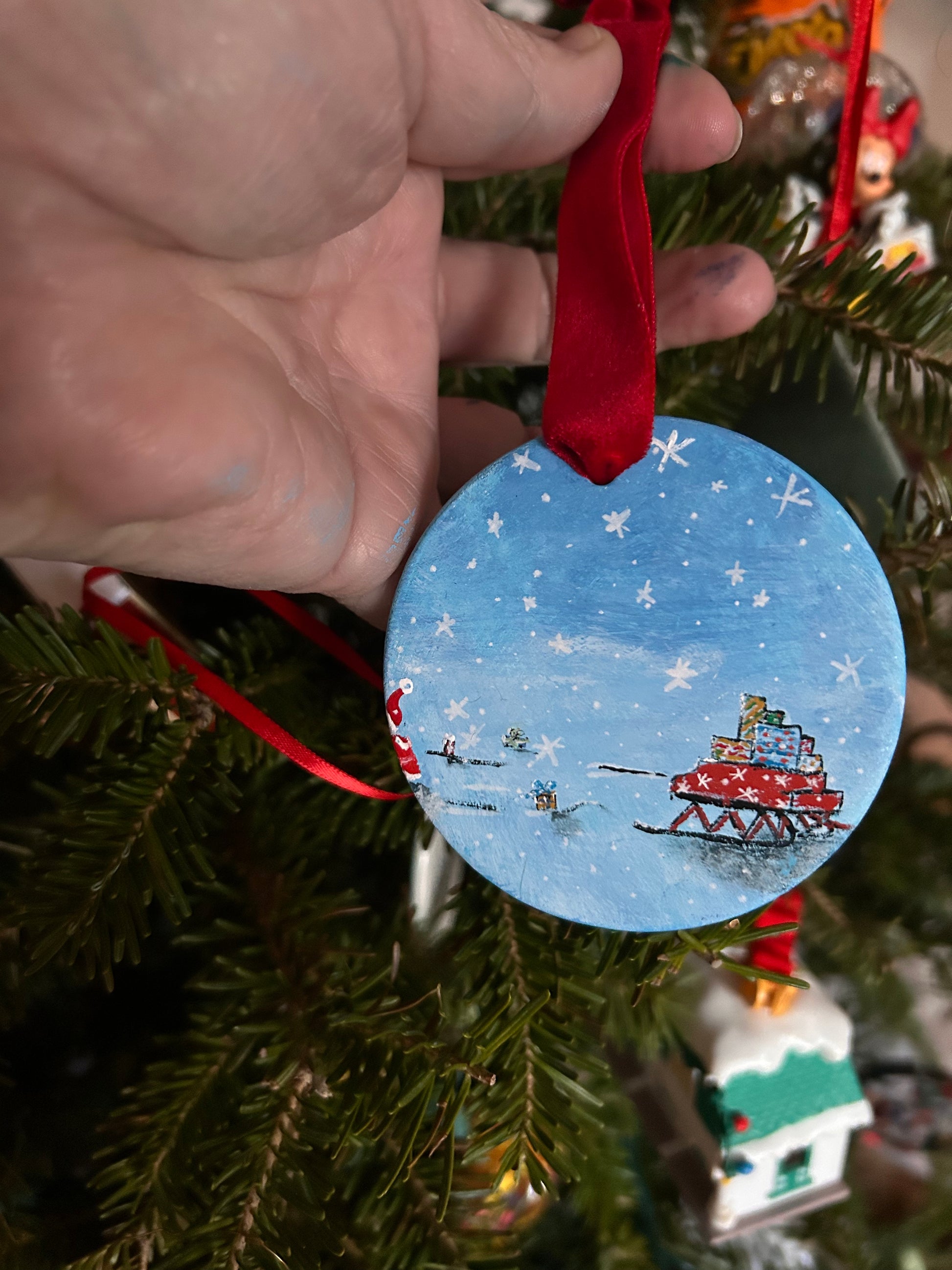 Original, hand-painted, round, flat Christmas ornament with a festive Santa design hanging on a tree.