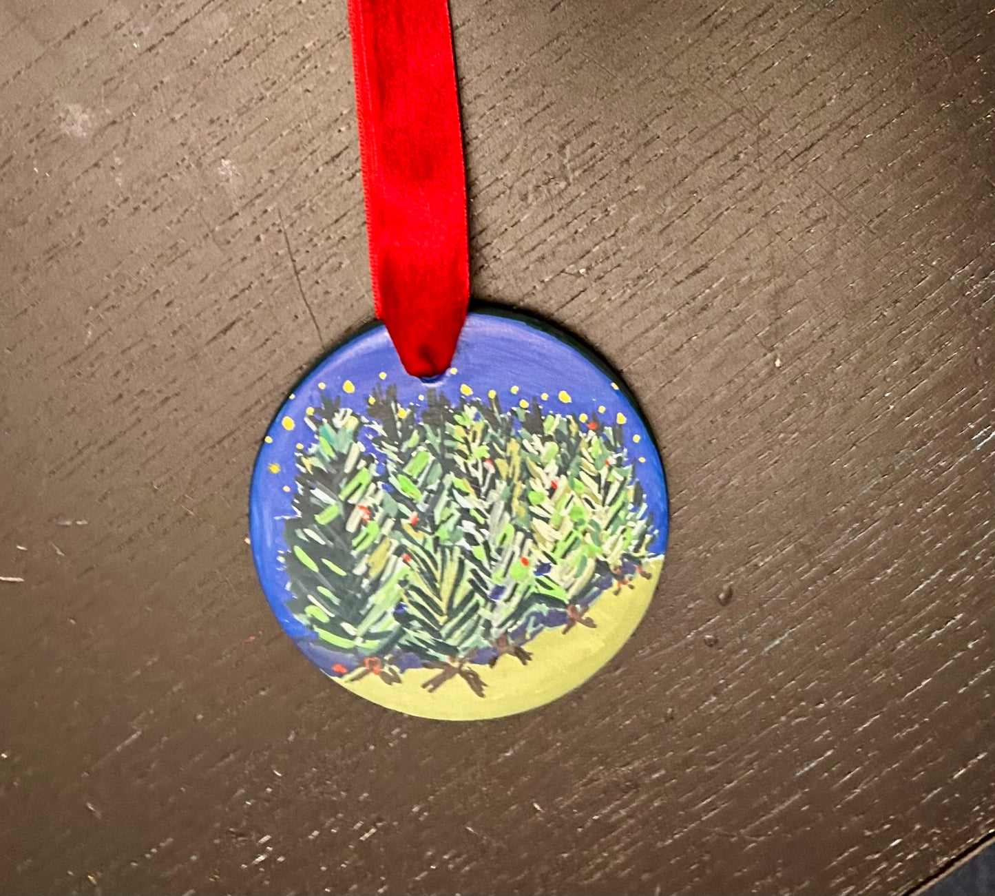 Decorative ornament with a blue background and Christmas trees design, hanging on a red ribbon.